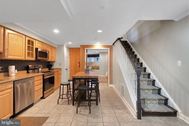 kitchen with appliances with stainless steel finishes, a breakfast bar area, light brown cabinetry, and light tile patterned floors