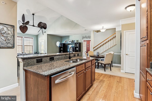 kitchen with sink, dark stone counters, a kitchen island with sink, stainless steel dishwasher, and light wood-type flooring