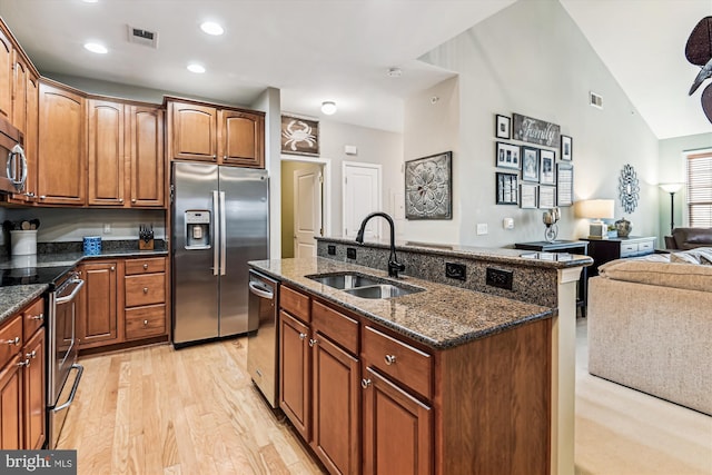 kitchen with lofted ceiling, sink, appliances with stainless steel finishes, an island with sink, and dark stone counters