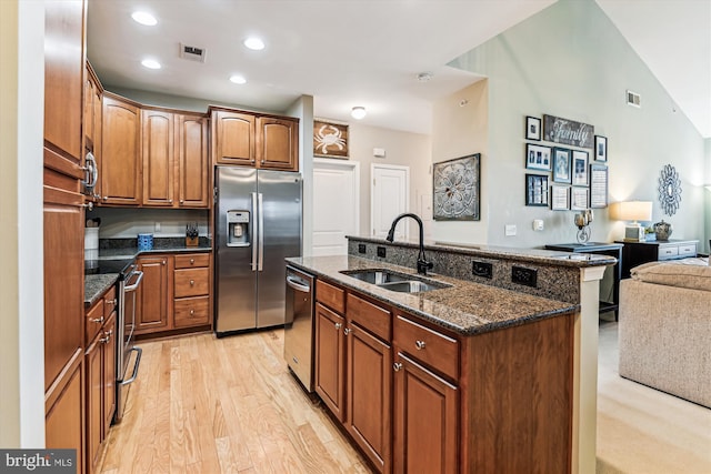 kitchen featuring a kitchen island with sink, sink, dark stone countertops, and appliances with stainless steel finishes