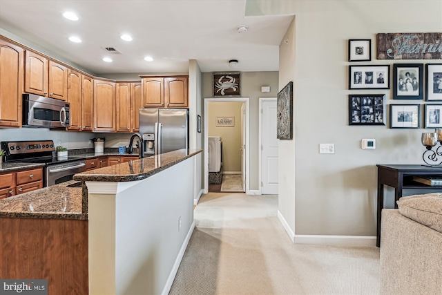 kitchen featuring appliances with stainless steel finishes, an island with sink, light carpet, and dark stone counters