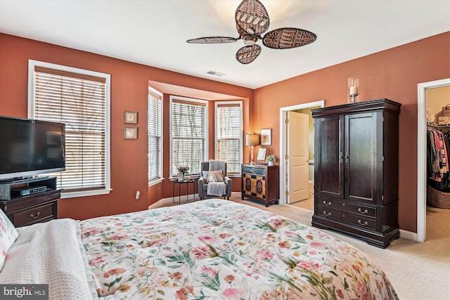 bedroom with a spacious closet, light colored carpet, a closet, and ceiling fan