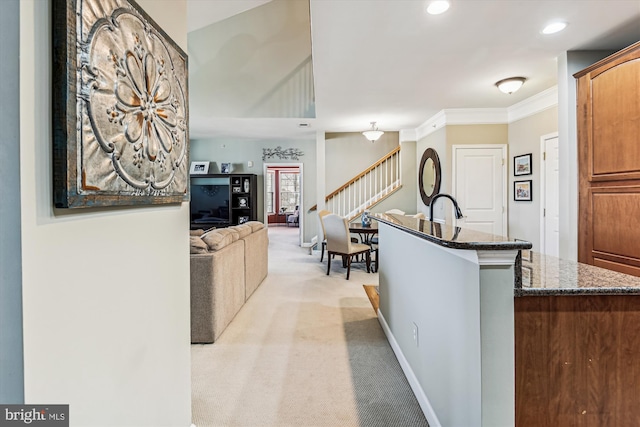 kitchen featuring sink, crown molding, dark stone countertops, an island with sink, and light carpet