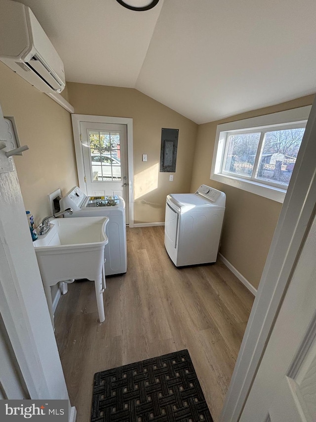 clothes washing area with sink, washer and clothes dryer, electric panel, an AC wall unit, and light wood-type flooring