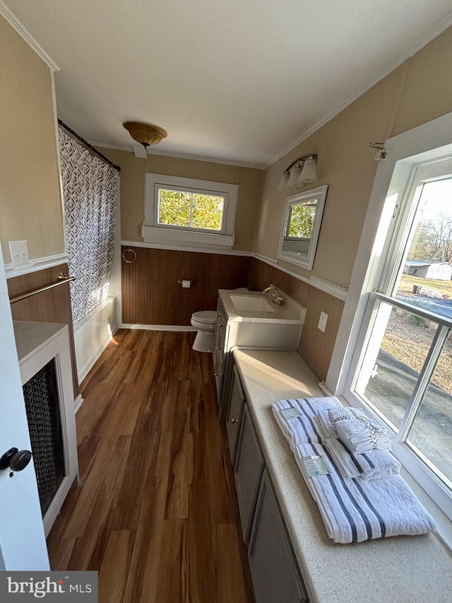 bathroom with hardwood / wood-style floors, wooden walls, ornamental molding, vanity, and toilet