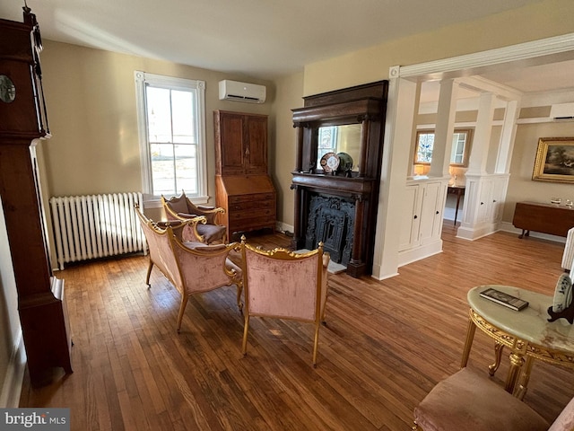 sitting room with a wall mounted air conditioner, hardwood / wood-style flooring, radiator heating unit, and decorative columns