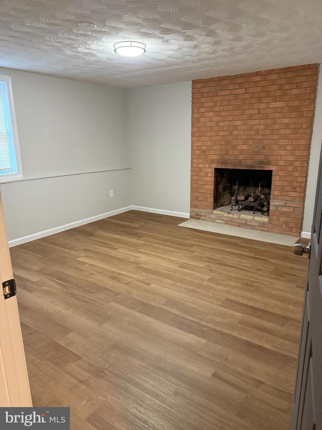 unfurnished living room featuring a brick fireplace, wood-type flooring, and a textured ceiling