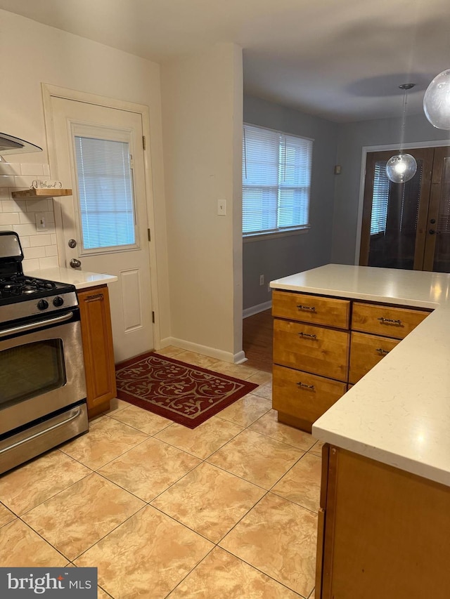 kitchen featuring light tile patterned flooring, stainless steel range with gas cooktop, decorative backsplash, and decorative light fixtures