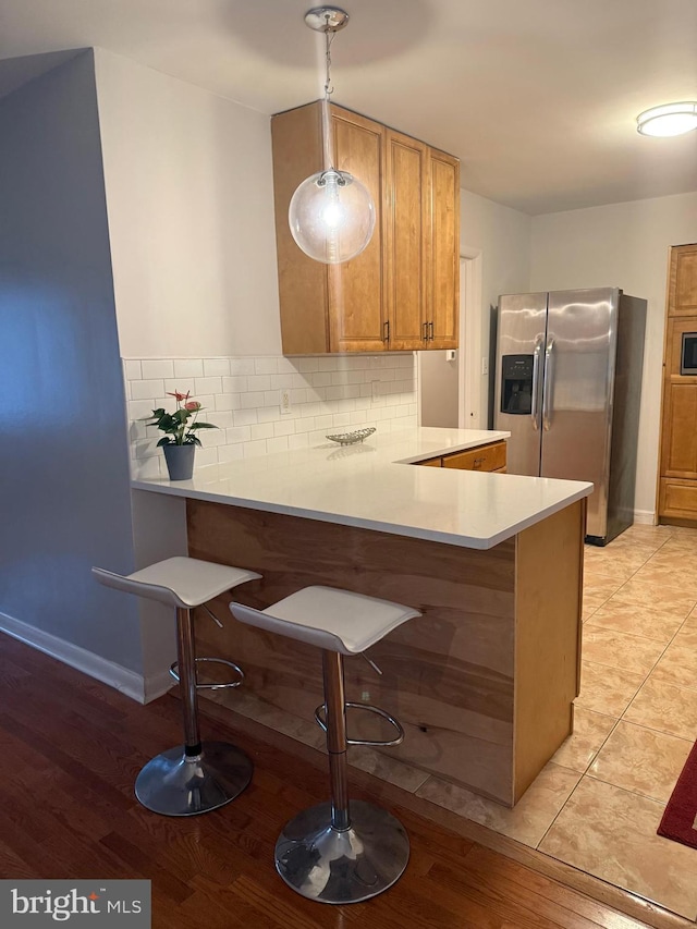 kitchen with a breakfast bar, decorative light fixtures, kitchen peninsula, stainless steel appliances, and backsplash