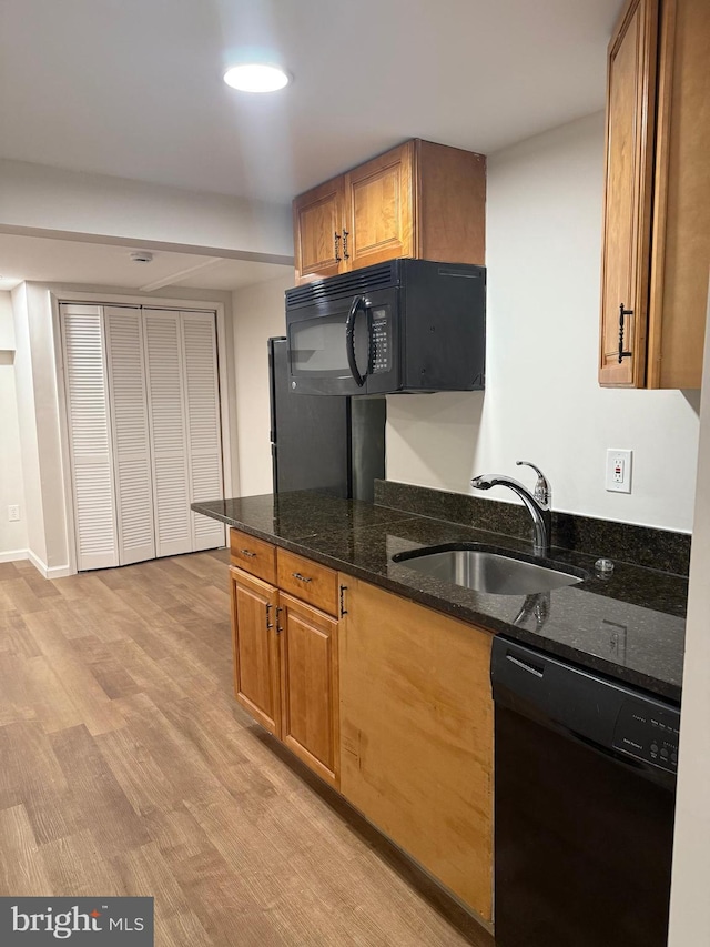 kitchen with light hardwood / wood-style floors, sink, dark stone counters, and black appliances