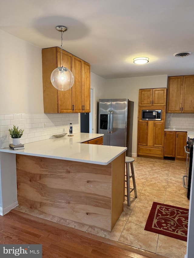 kitchen with a breakfast bar, appliances with stainless steel finishes, kitchen peninsula, pendant lighting, and decorative backsplash