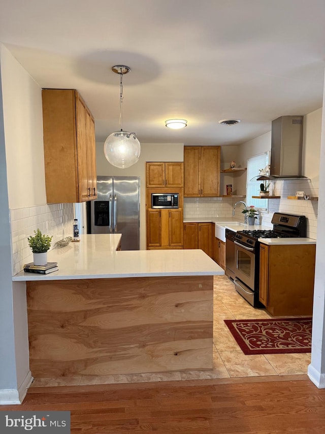 kitchen with stainless steel appliances, hanging light fixtures, wall chimney exhaust hood, and kitchen peninsula