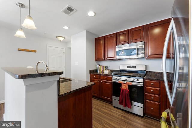 kitchen featuring decorative light fixtures, a center island with sink, dark stone counters, dark hardwood / wood-style floors, and stainless steel appliances