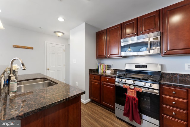 kitchen with stainless steel appliances, dark stone countertops, sink, and dark wood-type flooring