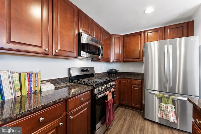 kitchen with dark wood-type flooring, stainless steel appliances, and dark stone counters