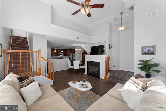 living room with ceiling fan with notable chandelier, ornamental molding, dark hardwood / wood-style floors, and a high ceiling