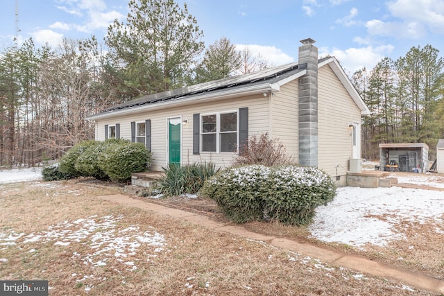 view of front of house featuring a chimney, an outbuilding, and roof mounted solar panels