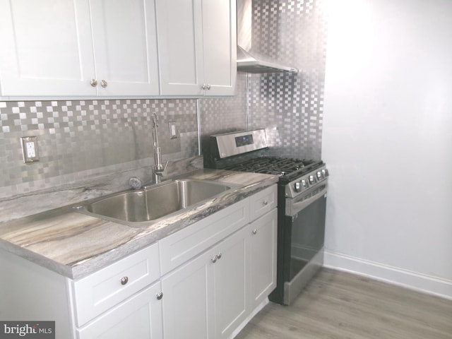 kitchen with white cabinets, sink, wall chimney range hood, and stainless steel gas range