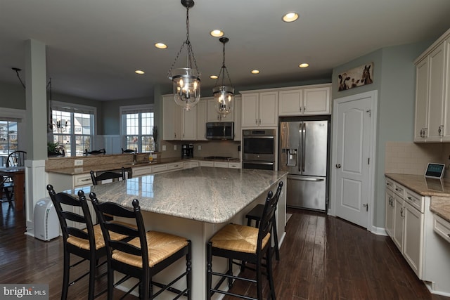 kitchen with a kitchen island, appliances with stainless steel finishes, pendant lighting, and light stone counters