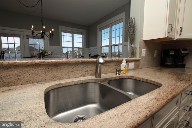 kitchen featuring sink, backsplash, white cabinets, hanging light fixtures, and light stone counters