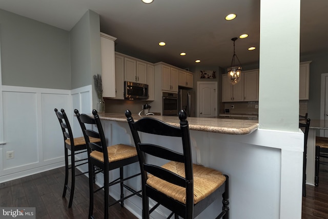 kitchen with appliances with stainless steel finishes, dark hardwood / wood-style floors, a breakfast bar area, and kitchen peninsula