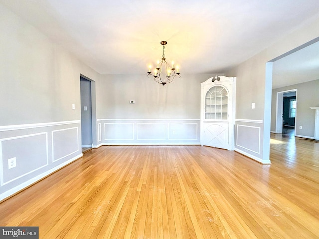 unfurnished room featuring an inviting chandelier and light wood-type flooring