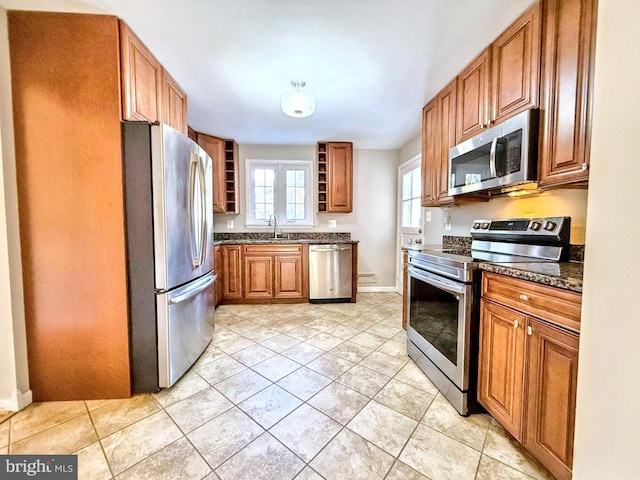 kitchen featuring stainless steel appliances, sink, light tile patterned floors, and dark stone counters