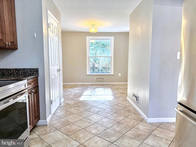 kitchen with stainless steel appliances, light tile patterned floors, and dark stone countertops