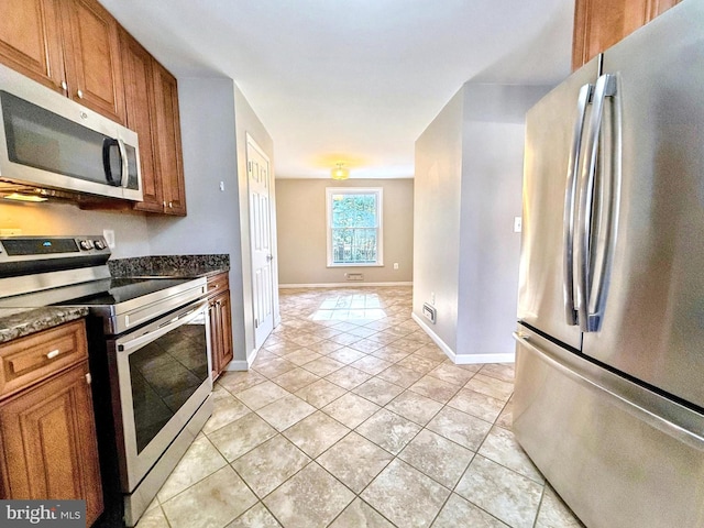 kitchen featuring light tile patterned flooring, dark stone counters, and appliances with stainless steel finishes