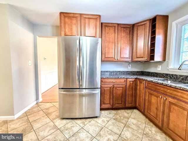 kitchen featuring dark stone countertops, sink, stainless steel fridge, and light tile patterned flooring