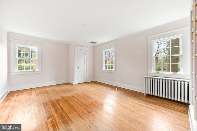 spare room featuring radiator, a wealth of natural light, and light hardwood / wood-style flooring