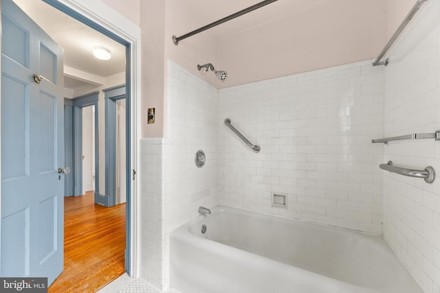 bathroom with tiled shower / bath combo, wood-type flooring, and tile walls