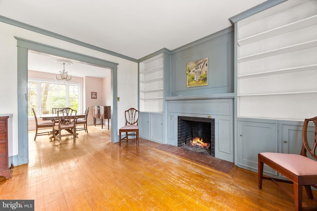 sitting room with light wood-type flooring, an inviting chandelier, a fireplace, and built in shelves