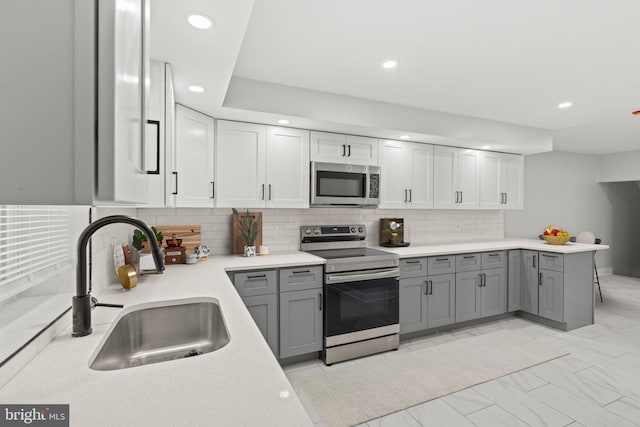 kitchen with gray cabinetry, stainless steel appliances, backsplash, sink, and kitchen peninsula