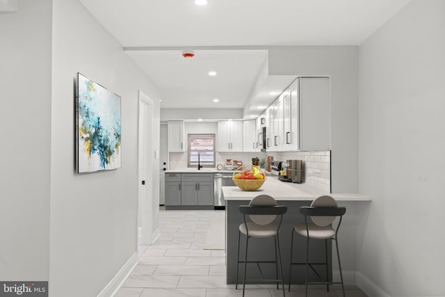 kitchen featuring kitchen peninsula, stainless steel appliances, white cabinets, a kitchen bar, and decorative backsplash