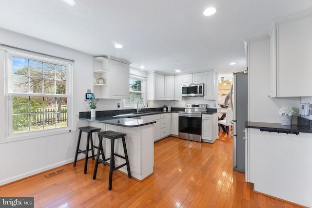 kitchen with light wood finished floors, visible vents, a peninsula, stainless steel appliances, and a sink