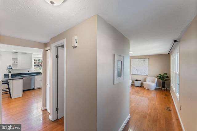 hallway featuring baseboards, visible vents, light wood finished floors, and a textured ceiling