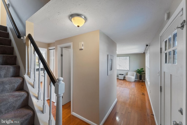 corridor with stairway, light wood-style flooring, a textured ceiling, and baseboards