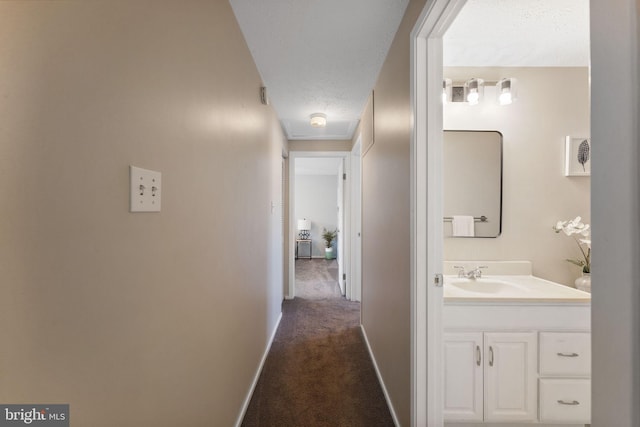 corridor featuring a textured ceiling, baseboards, dark carpet, and a sink