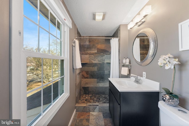 bathroom with stone tile floors, tiled shower, a textured ceiling, and vanity