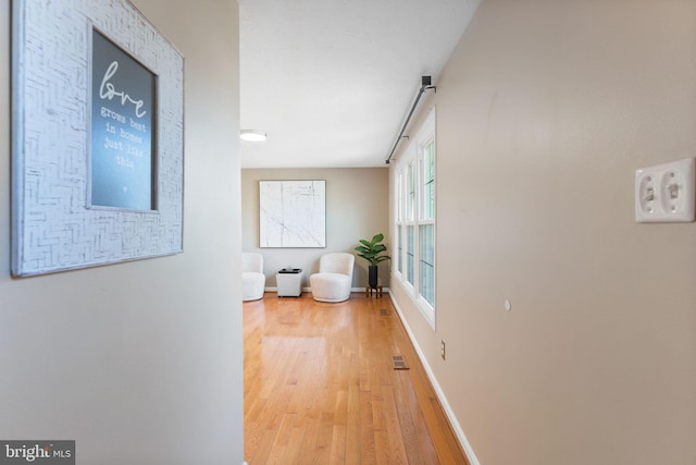 hall featuring visible vents, baseboards, and light wood-type flooring