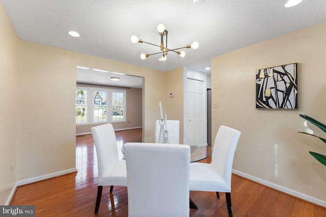 dining space featuring baseboards, a textured ceiling, an inviting chandelier, and hardwood / wood-style floors