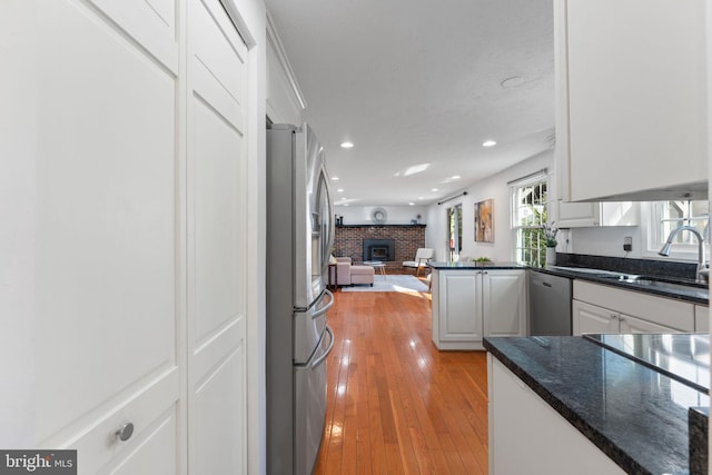 kitchen with open floor plan, a fireplace, light wood-style floors, stainless steel appliances, and a sink