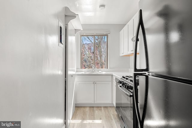 kitchen with sink, white cabinets, light wood-type flooring, and black appliances