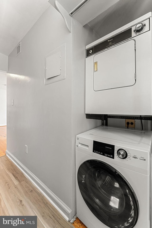 clothes washing area with stacked washer and clothes dryer and light wood-type flooring