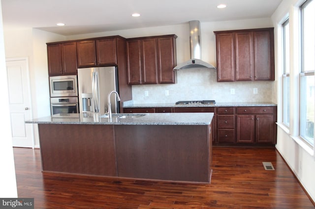 kitchen with appliances with stainless steel finishes, light stone countertops, sink, and wall chimney range hood