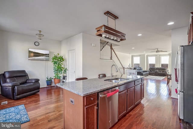 kitchen featuring sink, dark wood-type flooring, appliances with stainless steel finishes, light stone countertops, and an island with sink