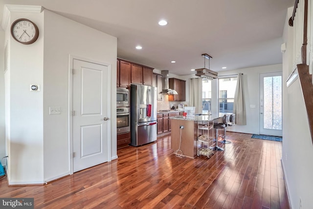 kitchen with wall chimney exhaust hood, a breakfast bar, appliances with stainless steel finishes, a kitchen island, and pendant lighting