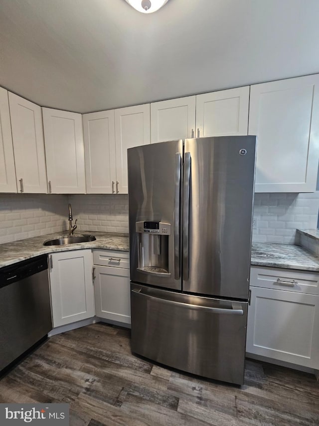 kitchen with sink, dark wood-type flooring, stainless steel appliances, light stone counters, and white cabinets