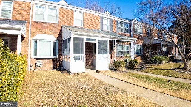 townhome / multi-family property featuring brick siding, a front lawn, and a sunroom